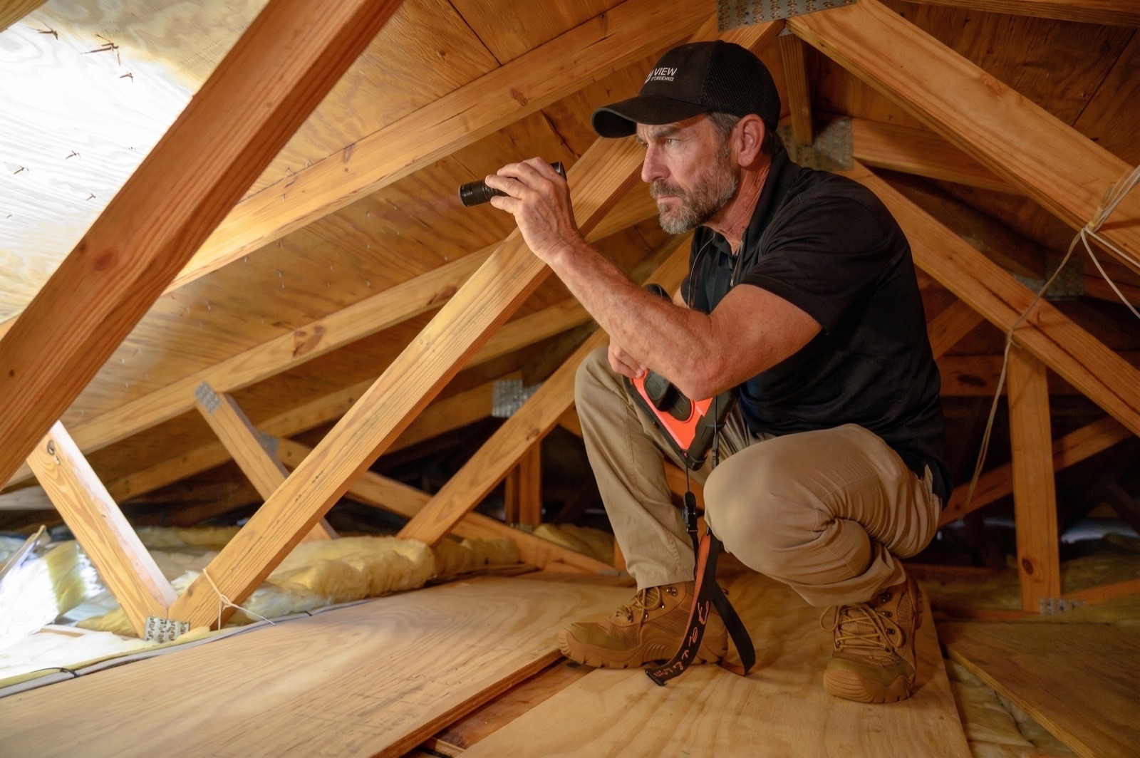 TruView Inspections home inspector examining attic framing and insulation with a flashlight during a Miami-area inspection